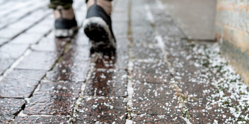 Kuva suolajyvistä jäisellä jalkakäytävän pinnalla talvella, jota käytetään jään ja lumen sulattamiseen.
